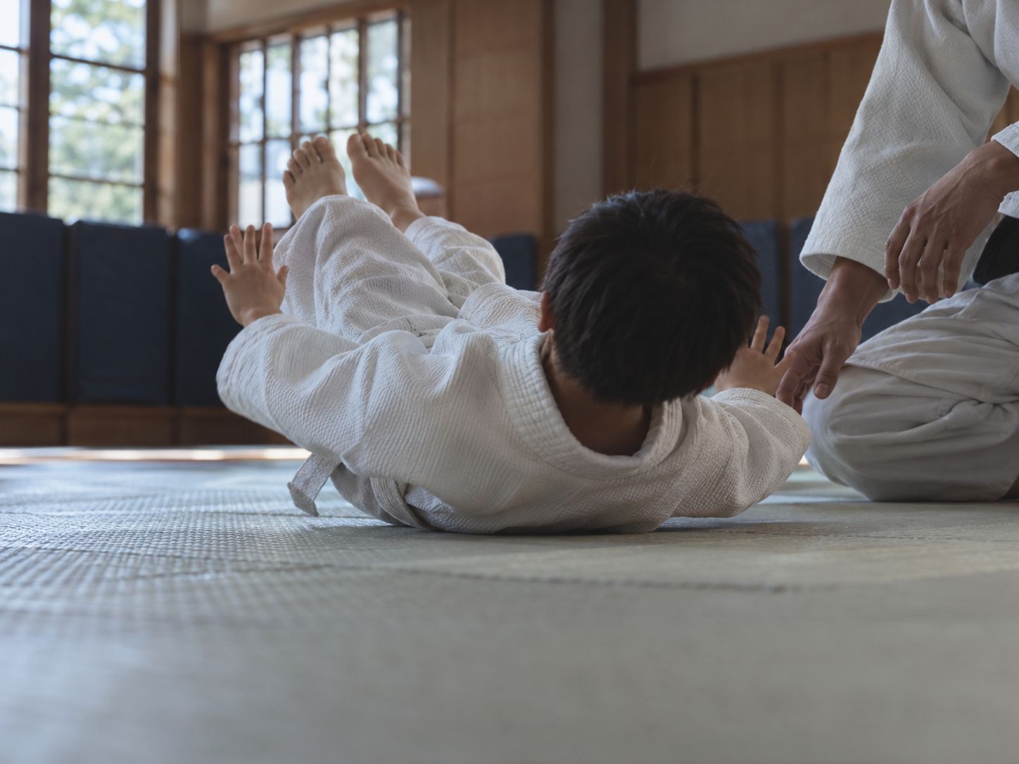 畳の上で受け身を練習する子どもと見守る先生